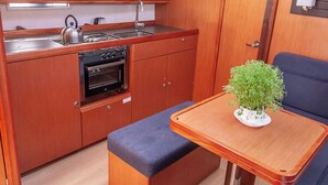 Een kleine kombuis met een kookplaat, oven en spoelbak; een klein bankje; en een bloempot op een tafel.