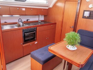 A compact galley with a stove, oven, and sink; a small bench; and a potted plant on a table. - Sun-Kissed Sailing Adventure in the Ionian Islands, Lefkada (Lefkada)