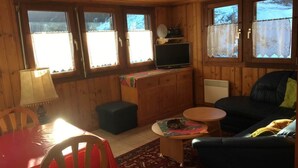 Un acogedor interior de cabaña con detalles de madera, un televisor sobre un mueble bajo, una mesa de comedor con sillas y un sofá.