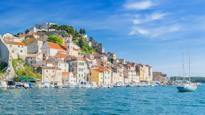 A coastal town with historic buildings, a harbor with boats, and a prominent castle on a hill.