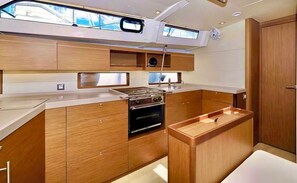 A compact kitchen with built-in appliances, wooden cabinetry, and a small window. - Sun-kissed Sailing Adventure in the Ionian Islands (Preveza)
