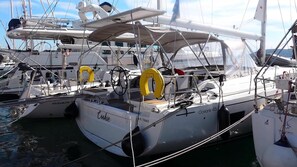 Un voilier est amarré dans une marina, on peut y voir des bouées de sauvetage, une cabine et un espace sur le pont.