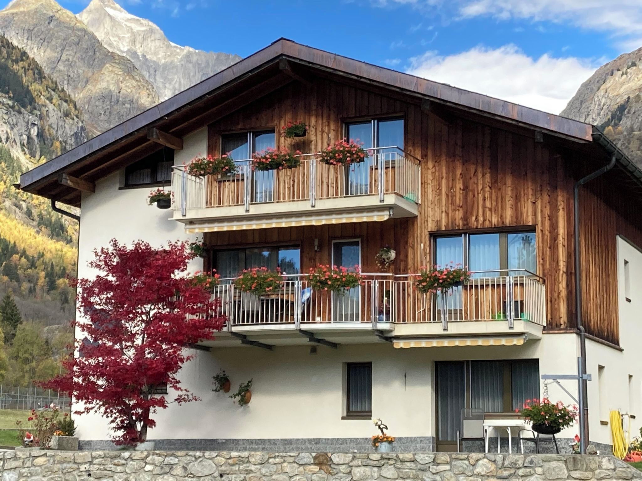 Un chalet en bois à deux étages, doté de balcons, de murs en pierre et surplombant un paysage montagneux.