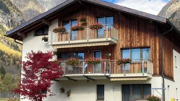 Un chalet en bois à deux étages, doté de balcons, de murs en pierre et surplombant un paysage montagneux.