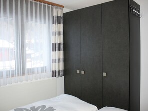 A bedroom with a bed, a wardrobe, and a window with curtains.
