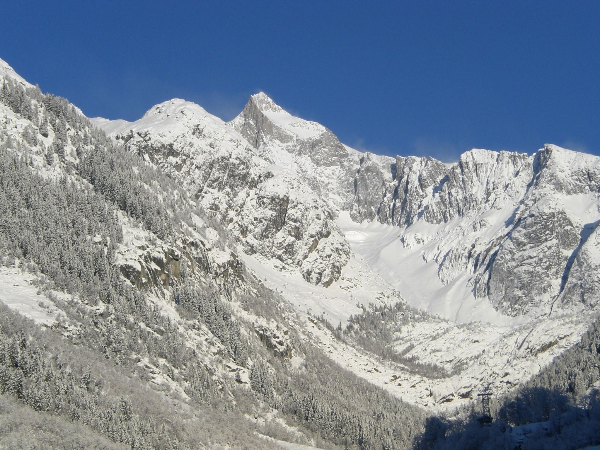 Un paysage montagneux aux sommets enneigés et aux arbres verdoyants.