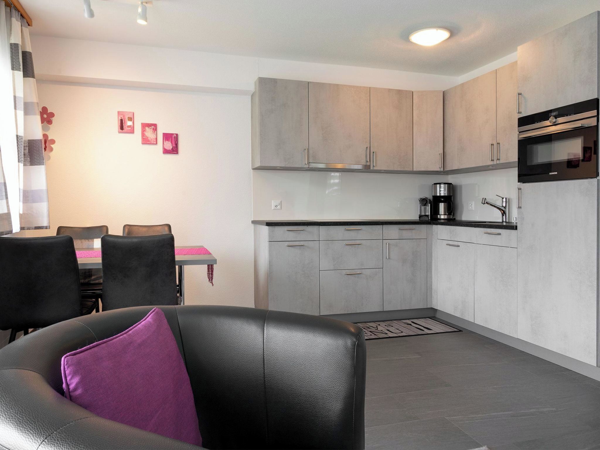 Une cuisine moderne avec des meubles gris, un plan de travail noir et un four Siemens.