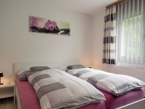 A double bed with a striped bedspread, a nightstand with a lamp, a window with sheer curtains, and a wall-mounted picture of an orchid.
