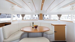 A boat interior with a round table, cushioned seating, and a small cabinet. - Sun-Kissed Sailing Adventure in Islas Sarónicas (Alimos)