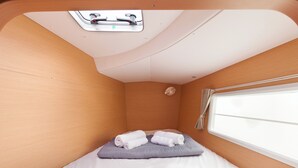 A compact room with a bed, a window with curtains, a skylight, and a small wall-mounted light fixture. - Sun-Kissed Sailing Adventure in Islas Sarónicas (Alimos)