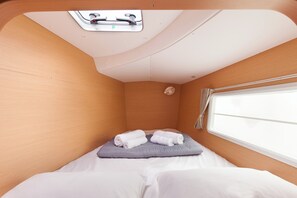 Ein kleines Zimmer mit einem Bett, einem fensterbelaubten Fenster, einem Dachfenster und einer kleinen Wandleuchte.