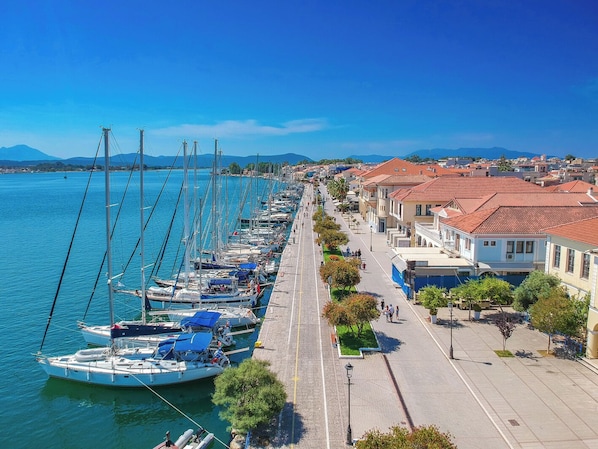 A marina with boats docked along a waterfront promenade, lined with buildings and trees.