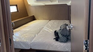 Interior compacto de uma RV, com uma cama, painel de controle para baterias e disjuntores, e uma pequena janela.
