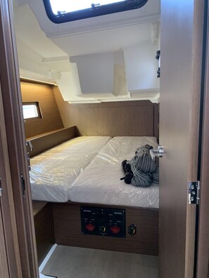 Ein kompaktes Wohnmobil-Interieur mit einem Bett, einer Bedienkonsole für Batterien und Sicherungen sowie einem kleinen Fenster.