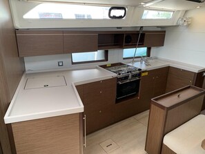 A compact galley with a stove, oven, and sink, wooden cabinetry, and a small window.