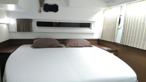 Una cama con cabecera, una mesita de noche, una ventana con cortinas y un equipo de aire acondicionado instalado en la pared.