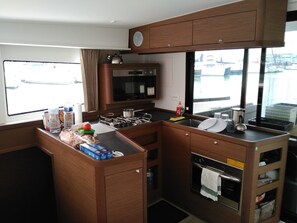 A compact kitchen with a microwave, stove, sink, and a window with a view of boats. - Caribbean Sun-Kissed Sailing: A Luxurious Beach Experience from Martinica, Le Marin (Le Marin)