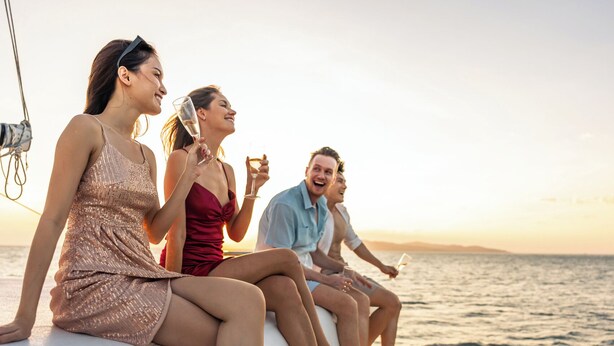 Um grupo de pessoas em um barco, com vista para o mar e um pôr do sol ao fundo.