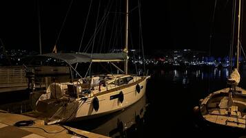Un port de plaisance de nuit, avec des bateaux amarrés, une vue sur la ville en arrière-plan et une vue dégagée sur l’eau.