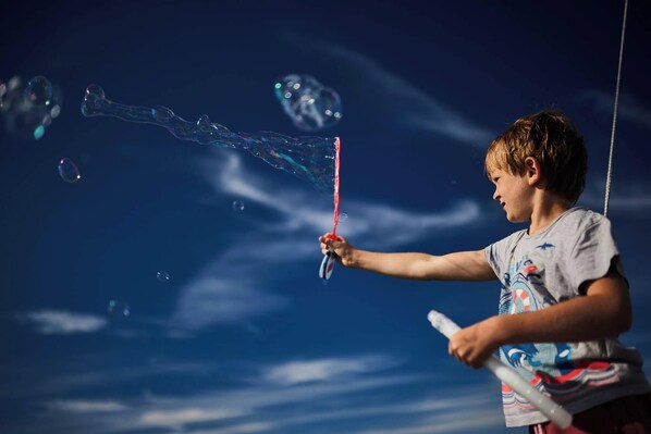 A child playing with bubbles against a clear sky.