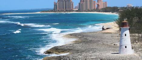 A coastal scene with a lighthouse, rocky shoreline, and a beachfront hotel complex.