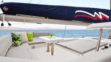 Ponte di una barca con zona coperta, cuscini, un piccolo tavolo e vista sul mare.