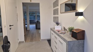 A modern interior with a hallway leading to a living area, a coat rack, a mirror, and a small plant on a counter.