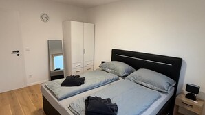 A bedroom with a bed, a wardrobe, a mirror, a clock, and a bedside table with a lamp.