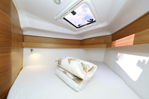 Quarto compacto com claraboia, cama com manta estampada e uma pequena mesa.