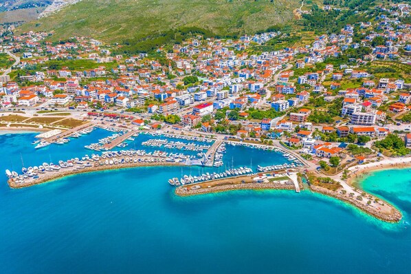 An aerial view of a coastal town with a marina, residential buildings, and hilly terrain in the background. - Sun-Kissed Sailing Adventure in Split-Dalmacia, Croatia (Podstrana)