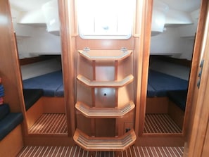 A compact interior with a central wooden shelf unit, two blue cushioned seating areas, and a small window at the top. - Sun-Kissed Sailing Adventure in the Ionian Islands, Lefkada (Lefkada)