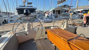 A boat deck with a wooden table, steering wheel, and multiple boats docked in the background. - Sun-Kissed Sailing Adventure in Sibenik, Croatia (Rogoznica)