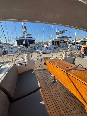 Ein Bootsdeck mit Holztisch, Steuerrad und mehreren im Hintergrund liegenden Booten.