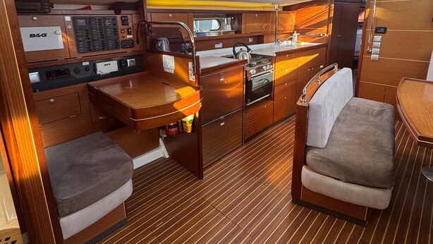 A compact kitchen with wooden cabinetry, a stove, and a sink. There are two cushioned seating areas and a small table. - Sun-Kissed Sailing Adventure in Sibenik, Croatia (Rogoznica)