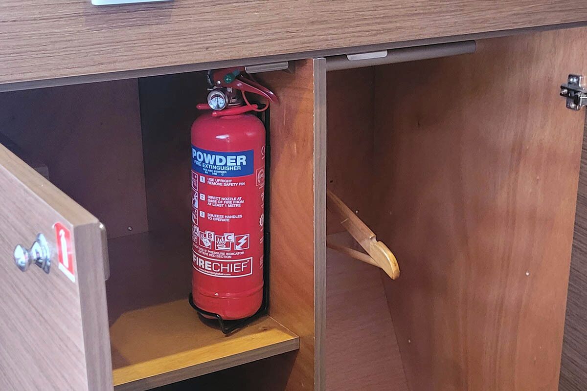 A fire extinguisher mounted on a wooden cabinet with a metal handle.
