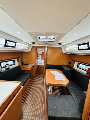 A compact interior with a central table, two couches, a small kitchenette, and a view through a door.