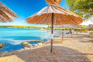 Ein Strand mit reetgedeckten Sonnenschirmen, klarem, blauem Wasser und einer felsigen Küstenlinie.