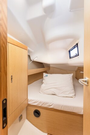 Cabine compacta e bem iluminada com beliche, uma pequena janela e um armário de madeira.