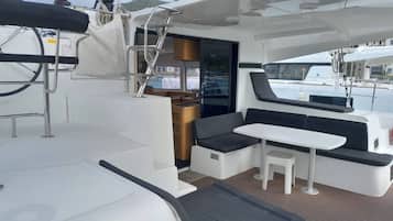 L'intérieur d'un yacht comprenant un espace repas, des sièges et une vue sur le port de plaisance.