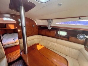 A compact interior with a wooden table, cushioned seating, a small window, and a fan. - Sun-Kissed Sailing Adventure in the Ionian Islands (Kontokali)