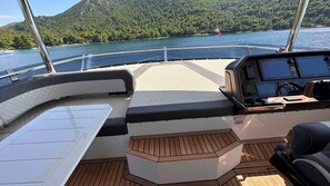 A boat's deck with a control station, cushioned seating, and a view of a lake with a forested island.