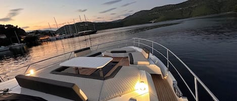 A boat deck with seating, a table, and a view of a marina and hills.