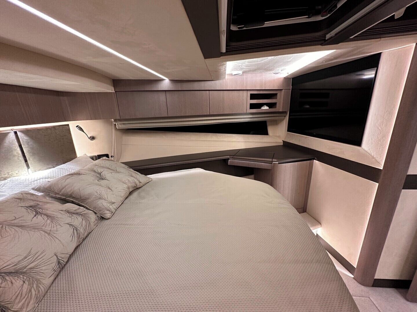 Ein kompaktes Wohnmobil-Interieur mit Bett, Küchenzeile und Fernseher.
