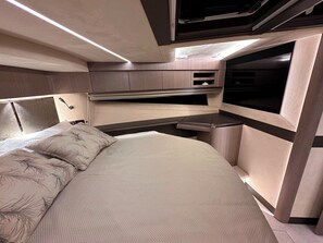 A compact RV interior with a bed, kitchenette, and a TV.