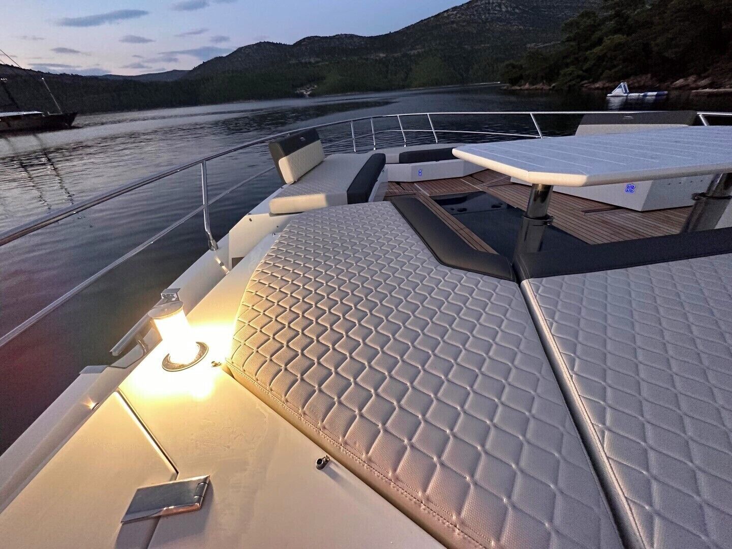 A boat deck with seating, a table, and a view of the water and hills.