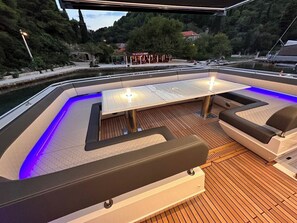 A boat deck with a table and seating, surrounded by water and greenery.