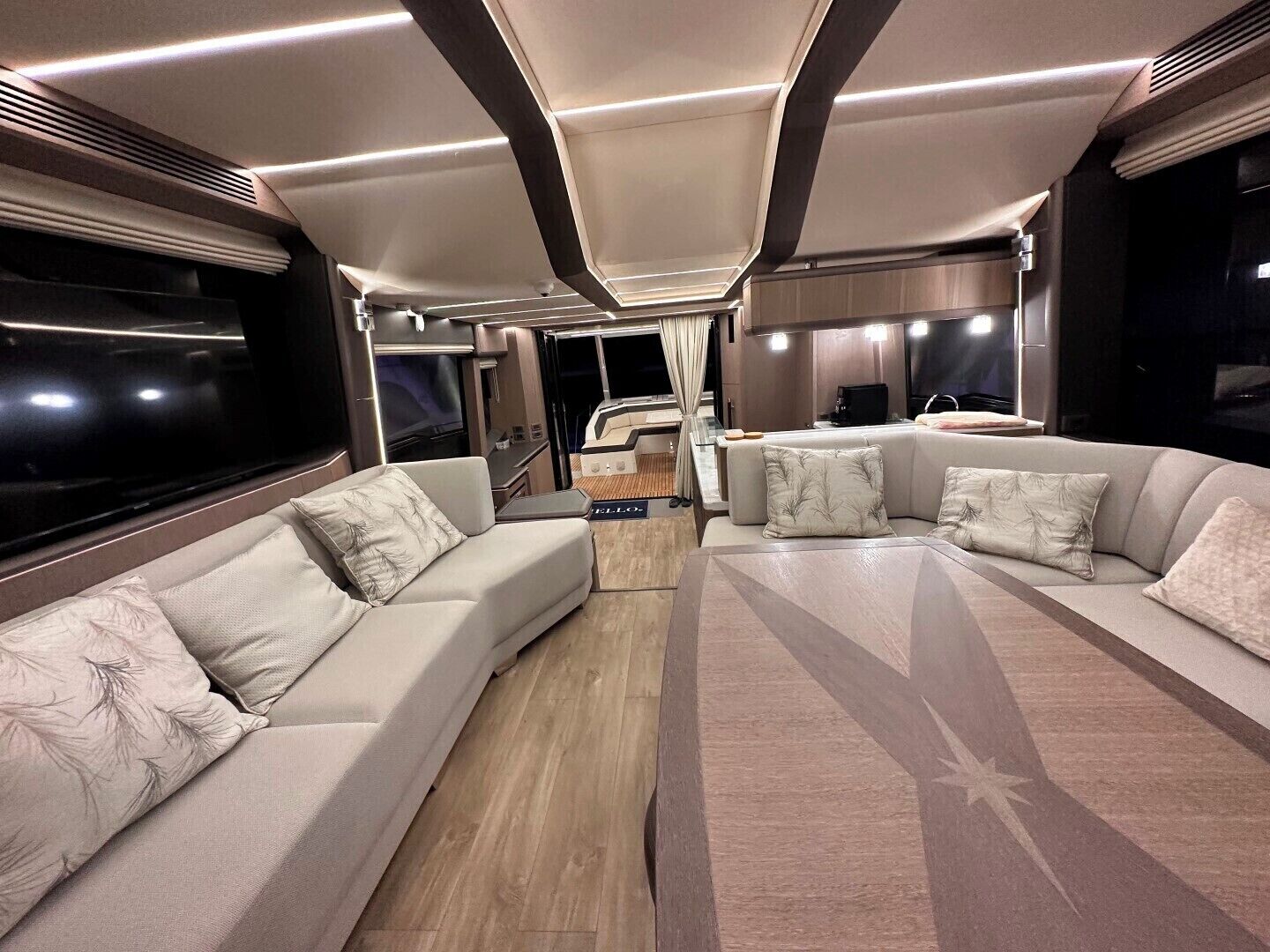 A modern RV interior with a sofa set, a dining table, and a kitchen area.
