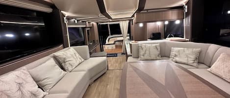 Un interior moderno de autocaravana con un conjunto de sofás, una mesa de comedor y una zona de cocina.