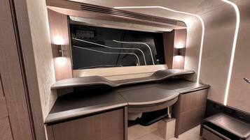 Un espace de travail moderne et bien éclairé, doté d’un bureau incurvé, d’étagères intégrées et d’un grand téléviseur à écran plat.
