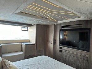 A compact interior with a bed, a seating area, a television, and a window.